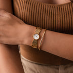 A person wearing the Brick Link Timepiece and a bold bracelet, paired with a brown ribbed tank top and beige pants.