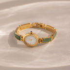 The Jade Band Timepiece features a minimalist oval dial, white face, and green jade link bracelet, displayed on a light textured surface.