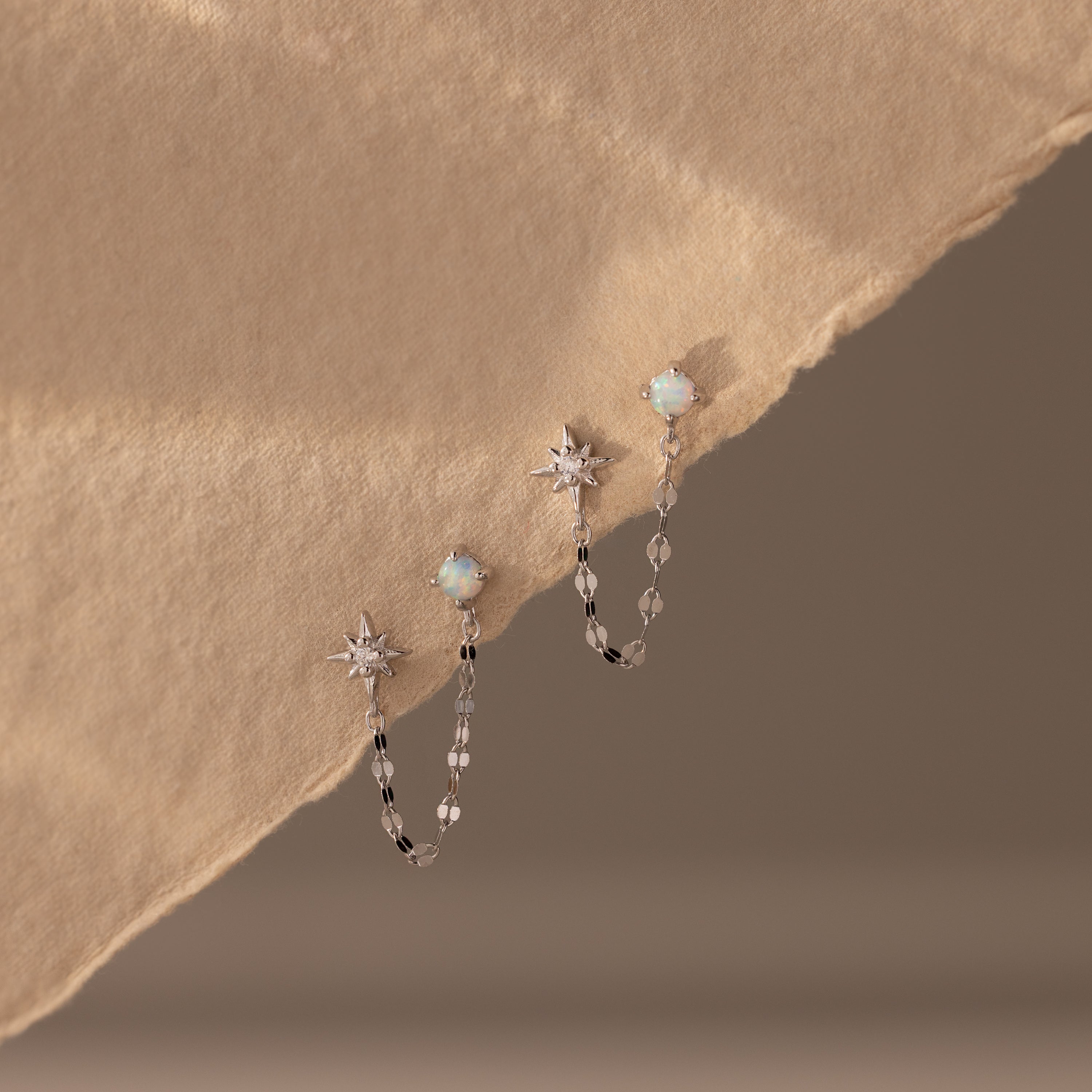 Flatlay of our Opal & Star Duo Chain Studs in Silver against a beige background