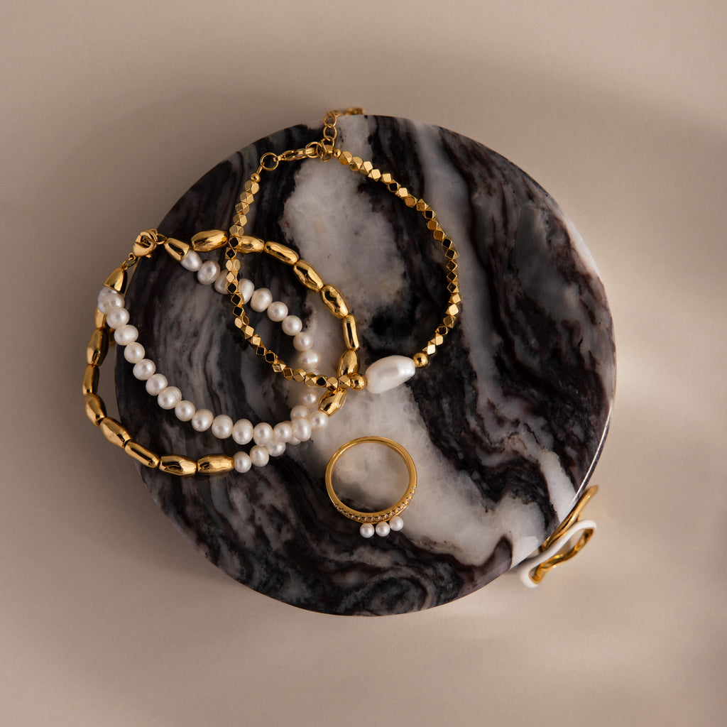 Gold and pearl jewelry pieces displayed on the Marble Jewelry Dish, which features a round design with a marbled black and white surface.