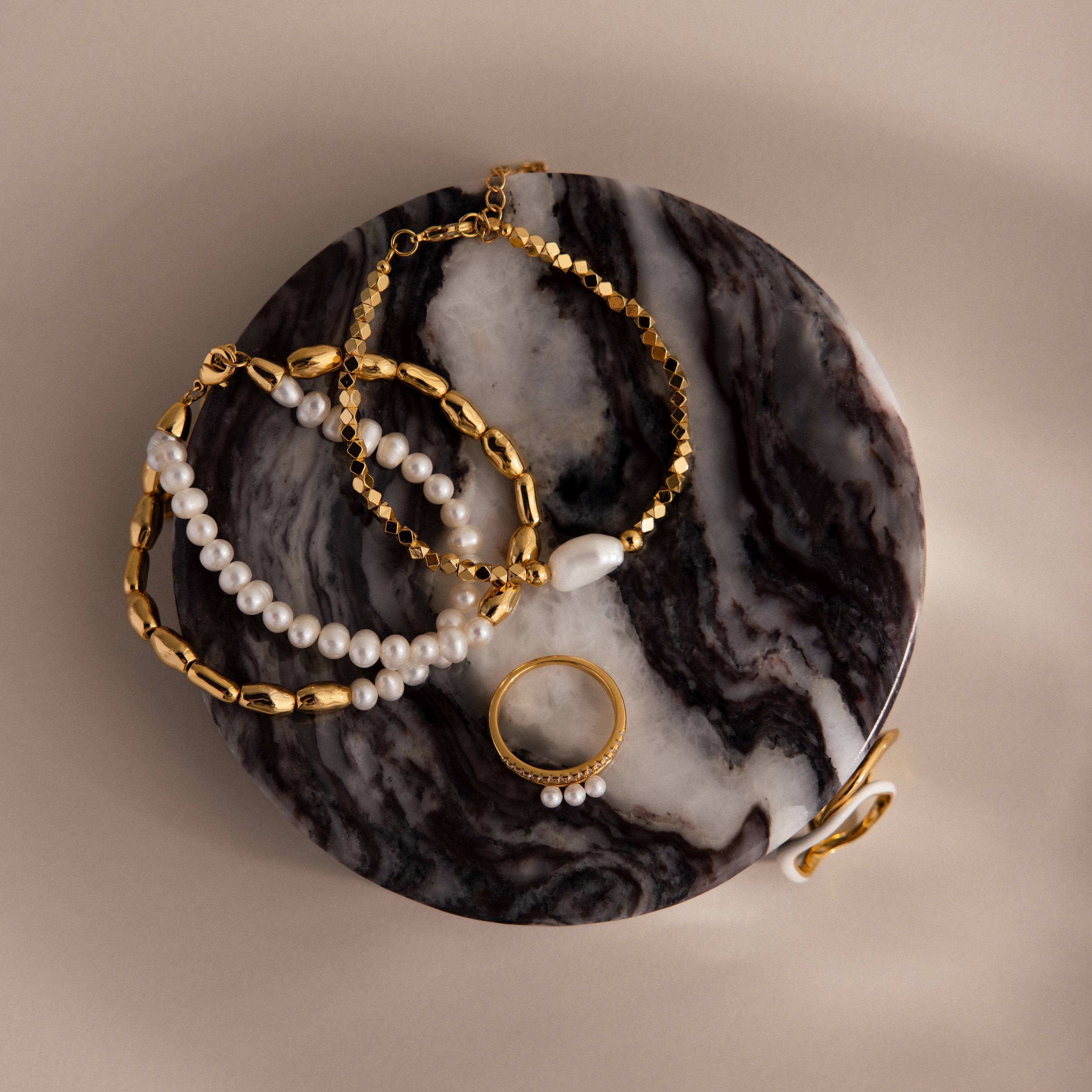 Gold and pearl jewelry pieces displayed on the Marble Jewelry Dish, which features a round design with a marbled black and white surface.