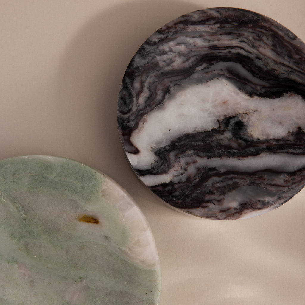 The Marble Jewelry Dish features two round marble slabs, one greenish and one dark with swirls, resting on beige—an elegant and stylish holder for your favorite jewelry pieces.