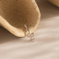 Sterling silver viper charm lying at the opening of a curved ceramic shell.