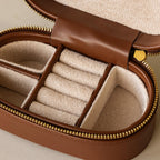 The Oval Leather Jewelry Box features a brown exterior, beige lining, ring slots, and section dividers—an ideal compact organizer to keep your jewelry neat and tidy.