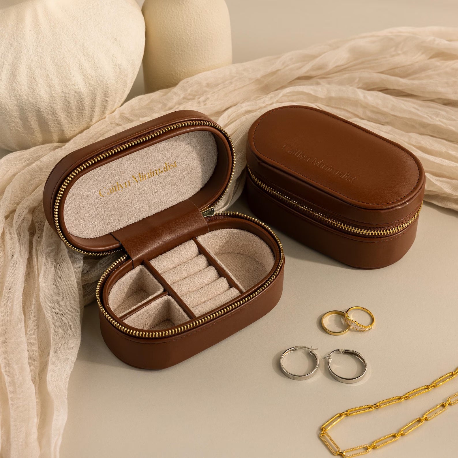 Two brown Oval Leather Jewelry Boxes, one open to show compartments with rings and a necklace nearby—ideal as a compact organizer or travel case for your jewelry.