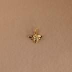 The Honeybee Charm in 18K Gold, adorned with small gemstones, is shown against a plain light brown background.