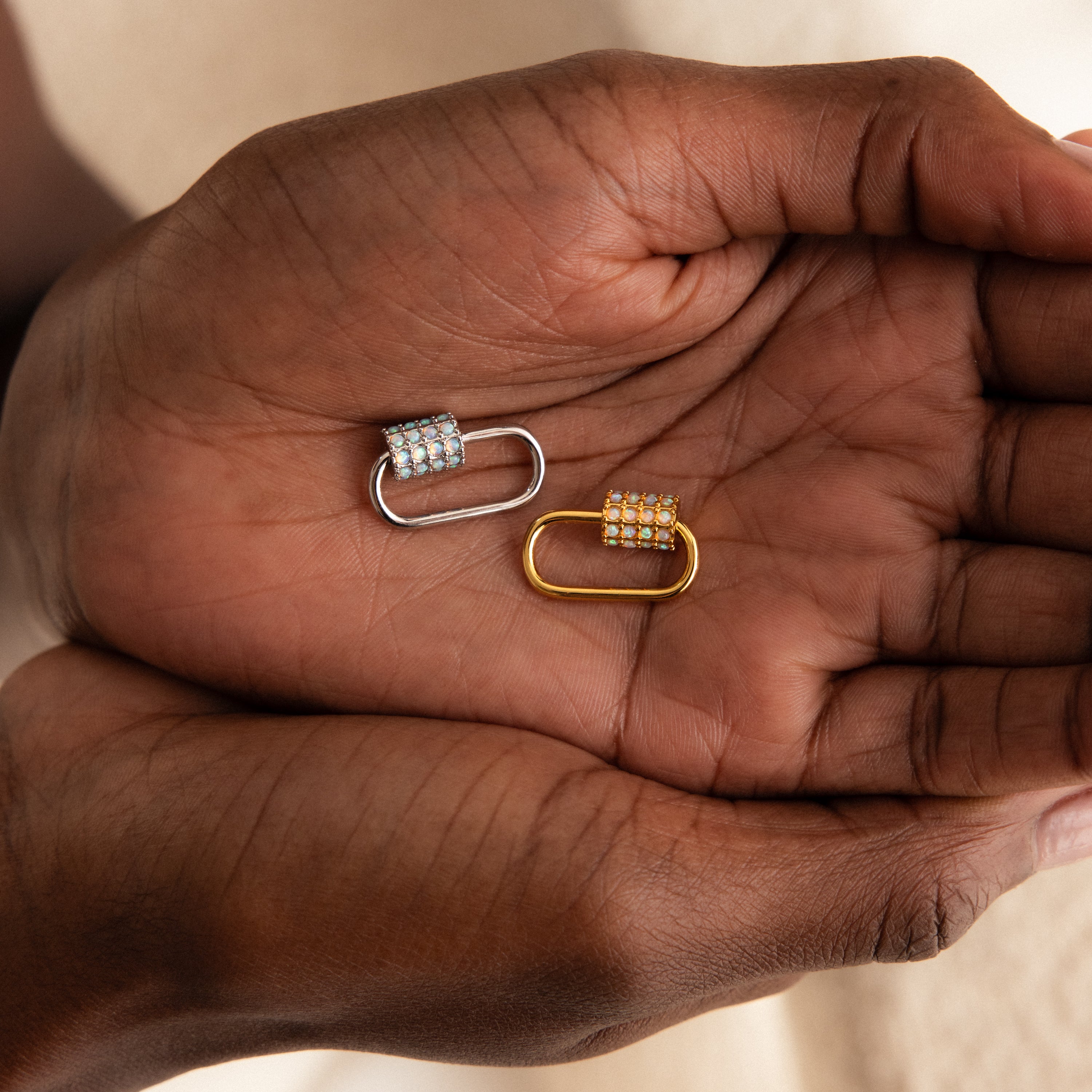 Two hands hold gold and silver gemstone-studded oval links side by side—ideal as the Opal Carabiner Clasp or a charm connector for your opal jewelry.