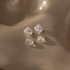 Heart & Flower Earring Backs in Sterling Silver—featuring clear heart and round silicone studs—rest on a smooth beige surface in soft lighting, ensuring secure and comfortable wear.
