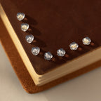 Eight small, translucent heart-shaped objects—similar to Heart & Flower Earring Backs in 18K Gold—line the corner of a brown, suede-covered book.