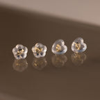 Four Heart & Flower Earring Backs with gold centers, shown on a reflective brown surface—stylish silicone stud backs for secure wear.