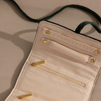 Open cream-colored Velvet Roll-Up Jewelry Case with gold zippers and buttons, lying on a beige surface with a visible green strap—an ideal stylish travel organizer for your jewelry essentials.