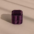 The Purple Flower Velvet Ring Box, a small purple box with a scalloped lid, sits on a beige surface with soft shadows.