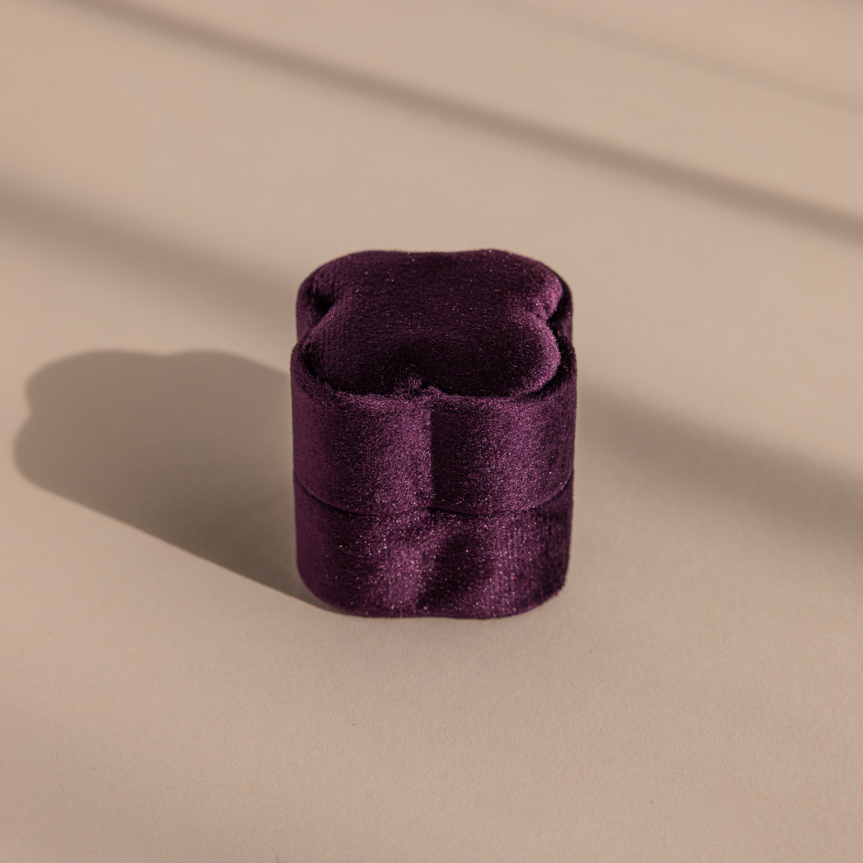 The Purple Flower Velvet Ring Box, a small purple box with a scalloped lid, sits on a beige surface with soft shadows.