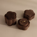 A Brown Flower Velvet Ring Box holds a delicate gold ring, with two matching closed boxes placed nearby.