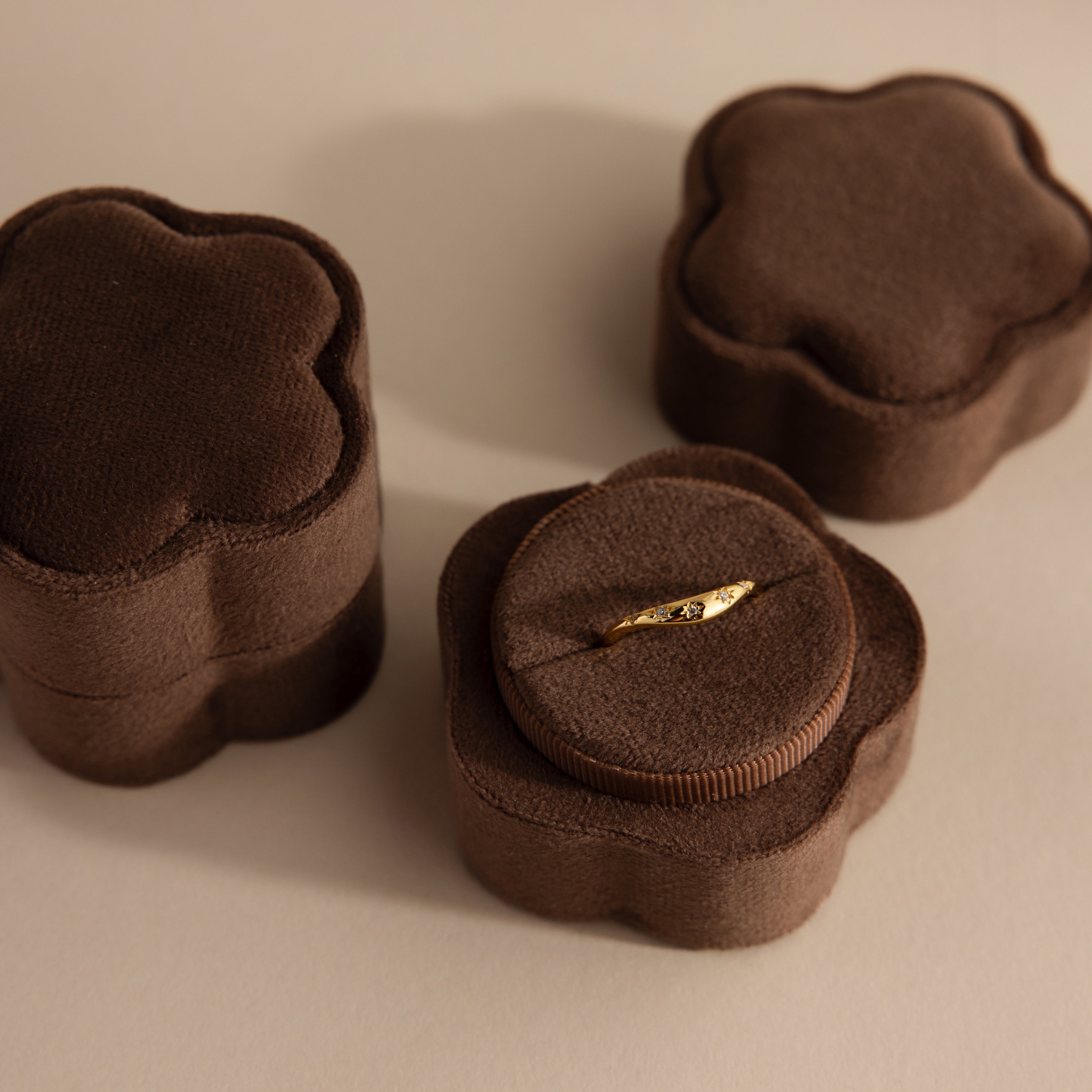 A gold ring sits in a Flower Velvet Ring Box—brown and flower-shaped—with two similar boxes beside it on a light surface.