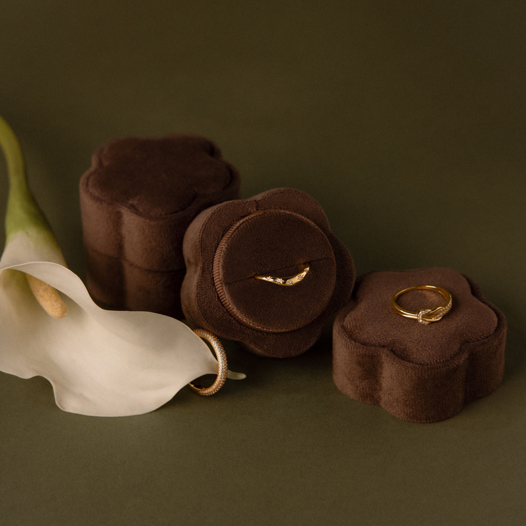 The Brown Flower Velvet Ring Box with a gold ring and calla lily sits elegantly on a green surface.