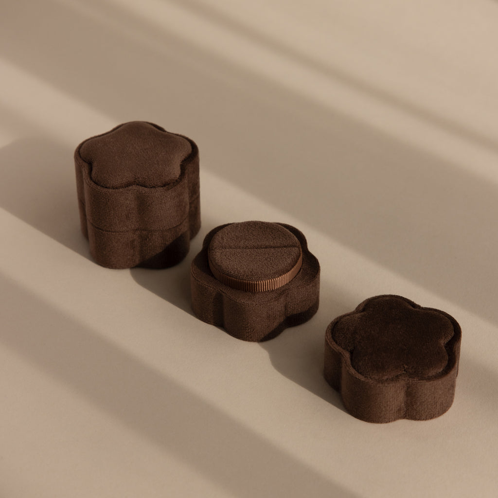 Three Brown Flower Velvet Ring Boxes, featuring a floral design and velvet finish, are arranged on a beige surface with soft shadows.