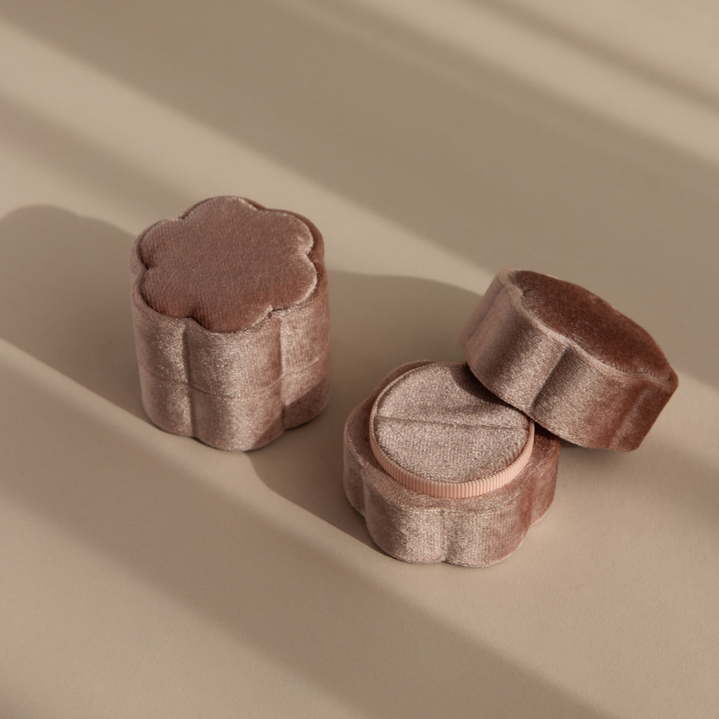 The Pink Flower Velvet Ring Box, shaped like a flower and crafted from soft pink velvet, rests on a beige surface with gentle shadows—an ideal choice for a romantic proposal.