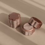 The Pink Flower Velvet Ring Box, shaped like a flower and crafted from soft pink velvet, rests on a beige surface with gentle shadows—an ideal choice for a romantic proposal.