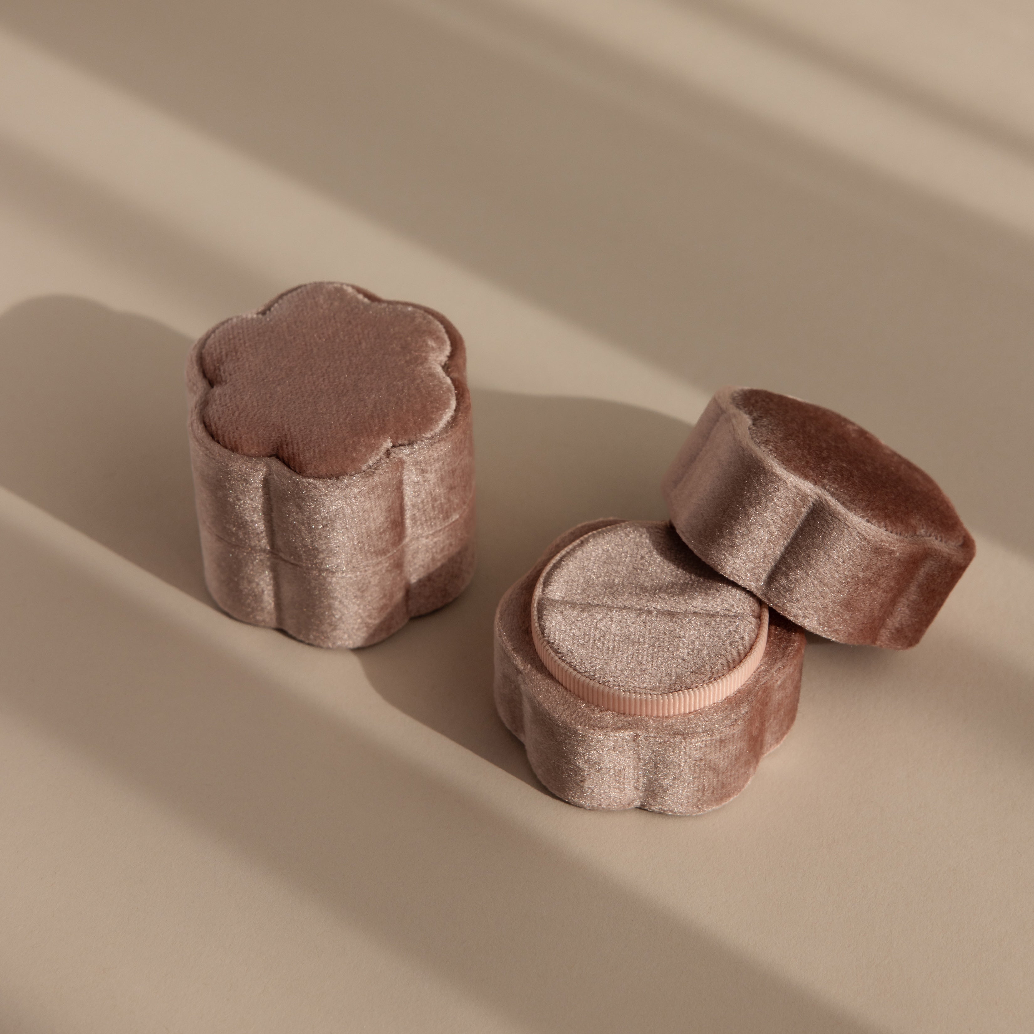 The Pink Flower Velvet Ring Box, shaped like a flower and crafted from soft pink velvet, rests on a beige surface with gentle shadows—an ideal choice for a romantic proposal.