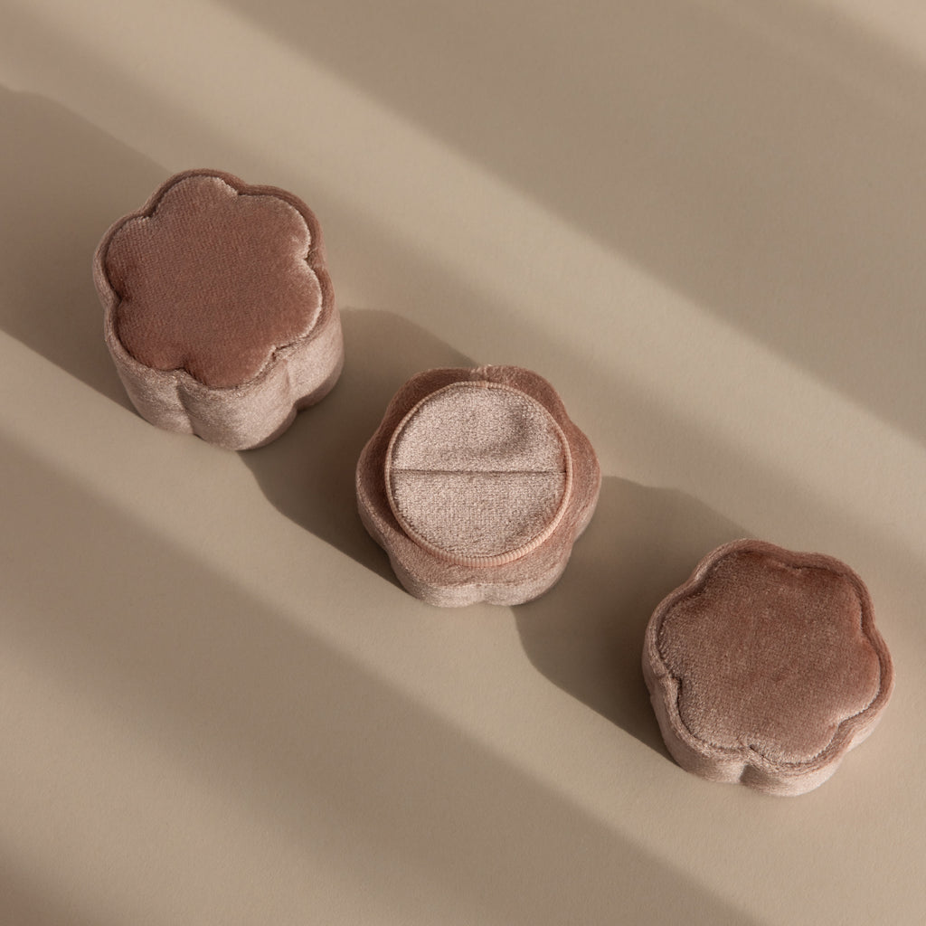 Three plush, flower-shaped puffs in soft brown tones are arranged on a beige surface, their appearance reminiscent of the Pink Flower Velvet Ring Box.