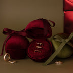 Three gold rings displayed in a Red Velvet Round Ring Box, with additional rings and ribbon-wrapped boxes nearby.