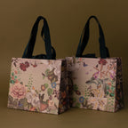 The Floral Gift Bag Add-On features two elegant floral-patterned gift bags with black handles, displayed on a simple olive green background.