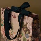 The Floral Gift Bag Add-On features elegant floral and bird designs with a dark ribbon bow handle—a perfect finishing touch for your gift wrapping.