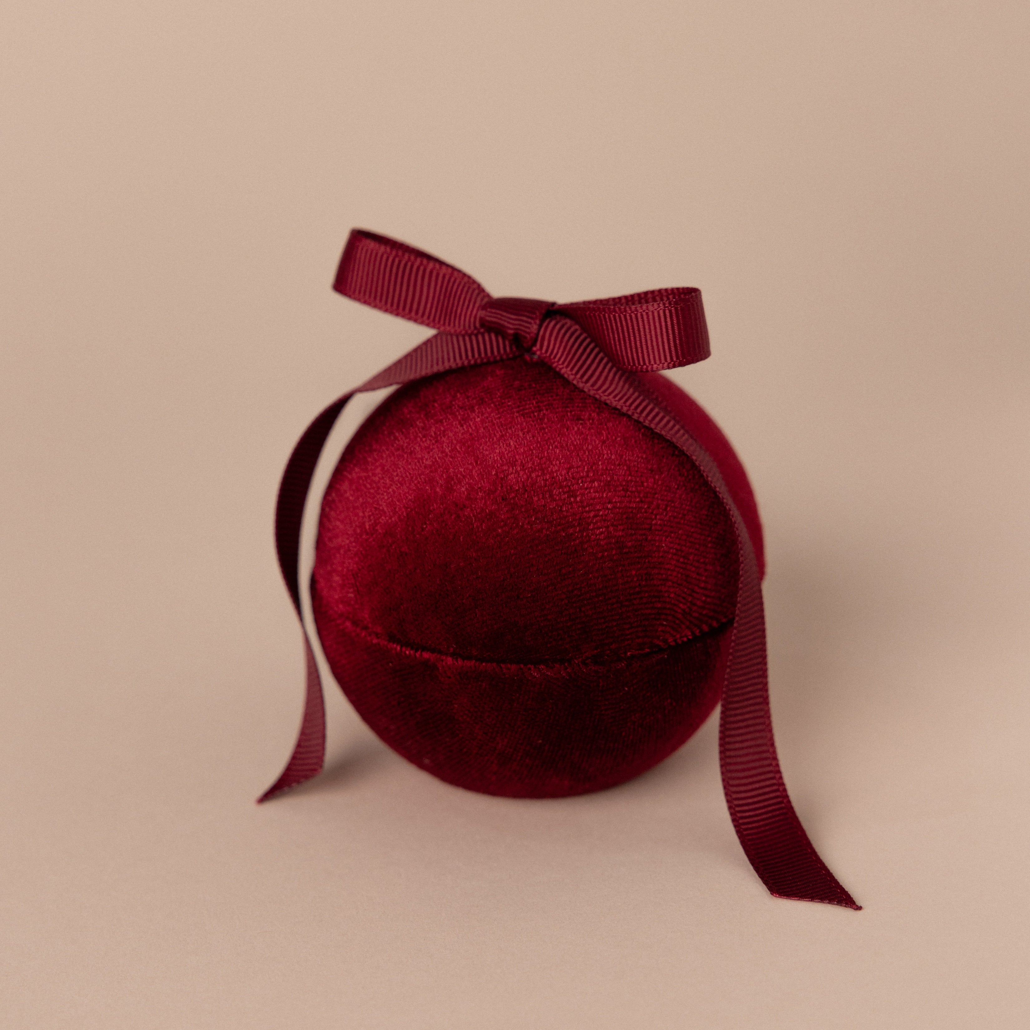 The Red Velvet Round Ring Box features a round shape with a matching ribbon bow, displayed on a beige background.