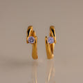 The Floating Alexandrite Huggies are gold hoop earrings with a curved design, each showcasing a single round alexandrite—ideal for those who love personalized jewelry.