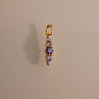 The Ombre Lace Amethyst Charm features five vertically arranged purple gemstones and casts a shadow on a beige background—an ideal personalized birth month gift.