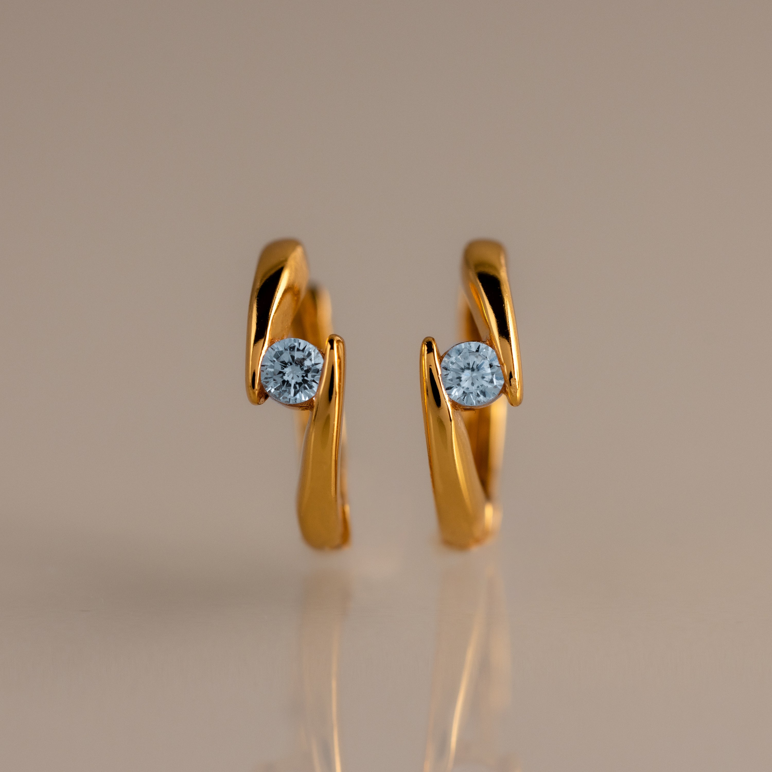 Floating Aquamarine Huggies: gold hoop earrings with a curved design, each set with a single round blue aquamarine—ideal for fans of personalized jewelry.