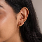 Close-up of a woman’s ear wearing Multiple Baguette Birthstone Huggies in Rose Gold—petite hoop earrings featuring pink gemstones—ideal for adding colorful style to any look.