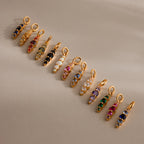 Twelve Ombre Lace Ruby Charm pendants, each with vibrant gemstone colors like birthstones, are neatly arranged on a beige surface.