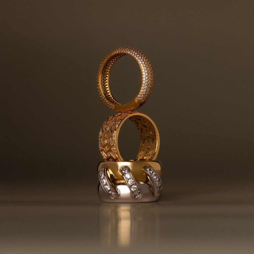 The Sculpted Mixed Metal Link Ring, adorned with pavé diamonds, is stacked with two other gold and diamond rings against a blurred brown background.