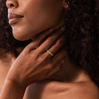 A woman touches her neck, displaying the Dainty Ribbed Alexandrite Ring on her finger against her bare skin and curly hair.