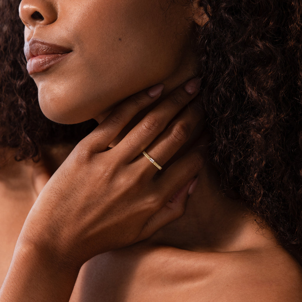 A woman touches her neck, showcasing the Dainty Ribbed Peridot Ring on her finger against her bare shoulder.