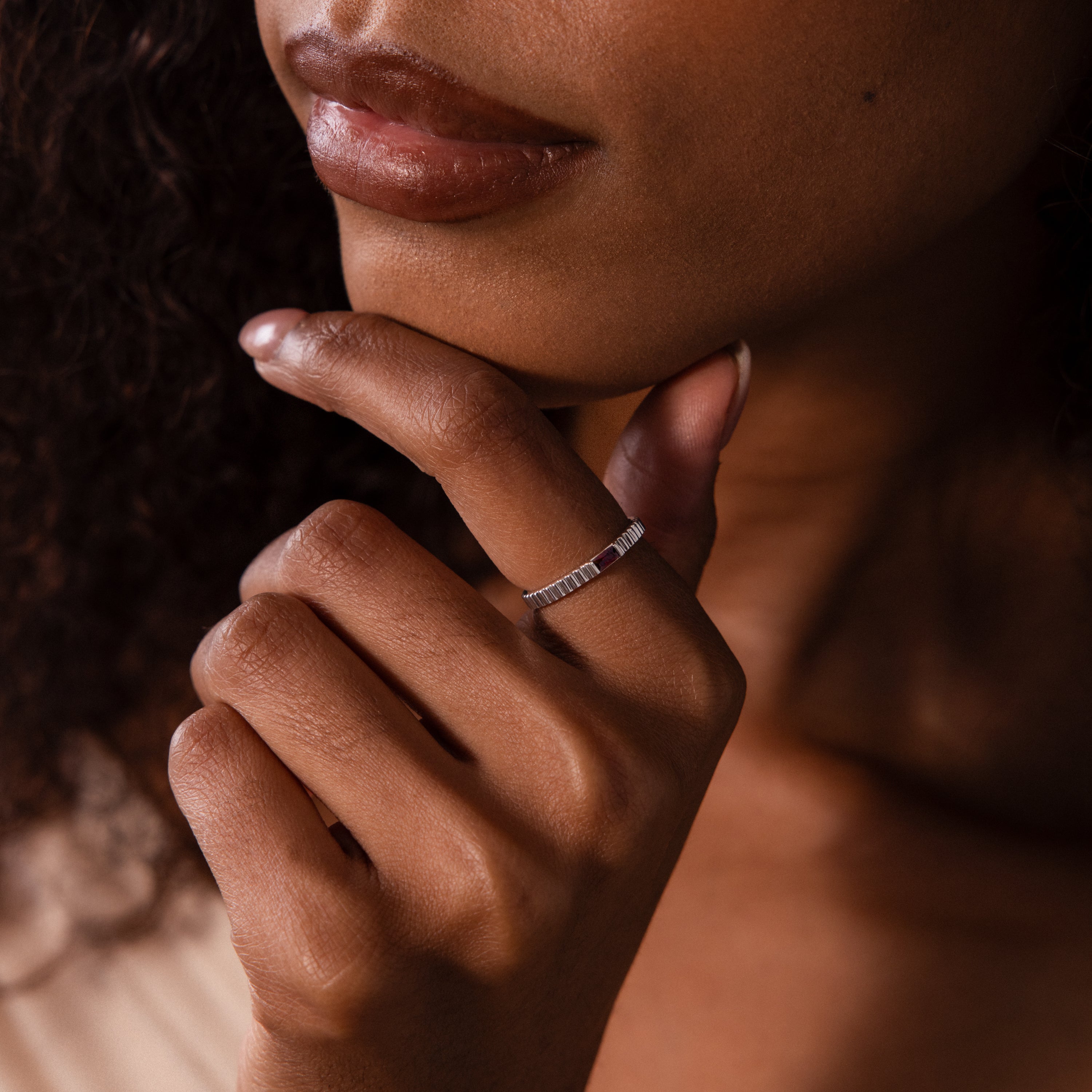 A woman with curly hair wears the Dainty Ribbed Topaz Ring—a slim silver band—on her finger, her hand resting near her chin.