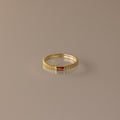 The Dainty Ribbed Garnet Ring features a ridged gold band with a small rectangular red gemstone, ideal as a delicate ring or personalized birthstone accessory, and is displayed on a neutral background.