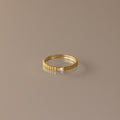 The Dainty Ribbed Diamond Ring features a slim gold ridged band and a petite rectangular diamond, perfect as a birthstone ring and shown on a neutral background.