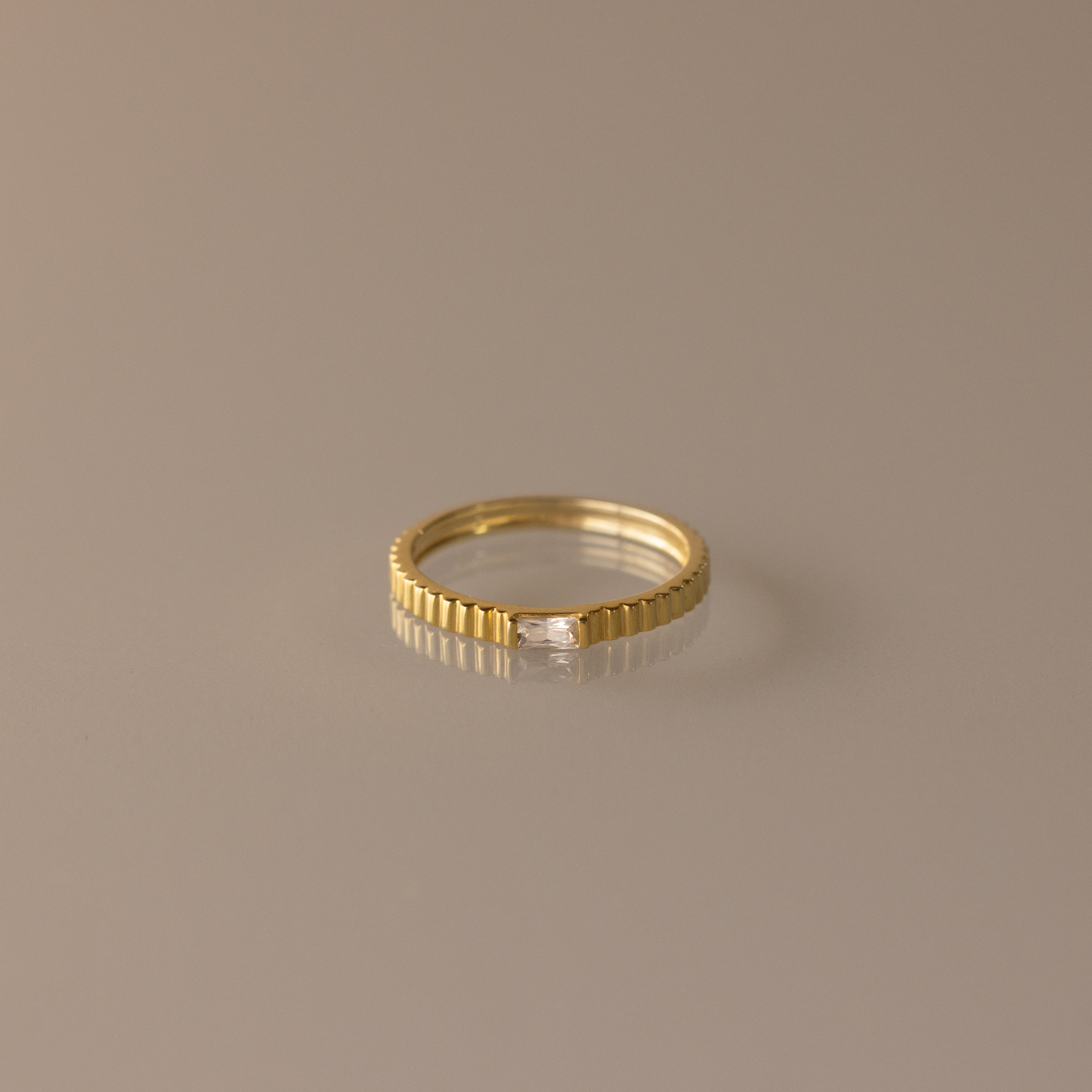The Dainty Ribbed Diamond Ring features a slim gold ridged band and a petite rectangular diamond, perfect as a birthstone ring and shown on a neutral background.