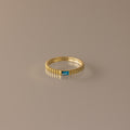 The Dainty Ribbed Blue Zircon Ring features a textured band and a small rectangular blue zircon gemstone, ideal as a birthstone piece or for stacking. Shown on a neutral background.