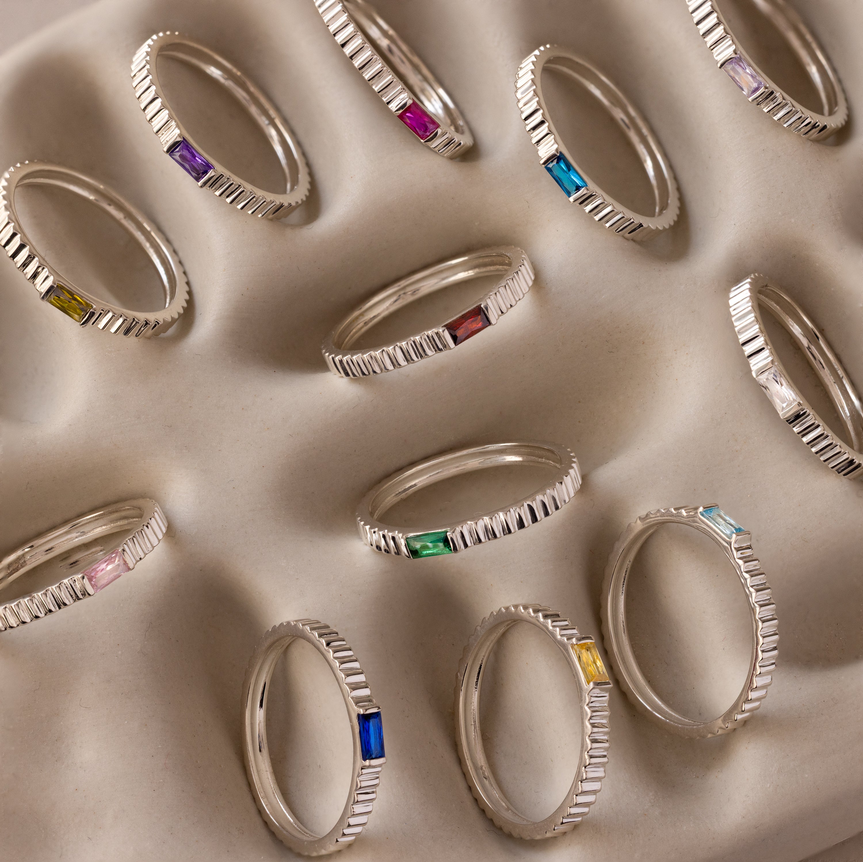 The Dainty Ribbed Diamond Ring is displayed on a wavy beige surface, its delicate design perfect for adding elegance or celebrating a special moment.