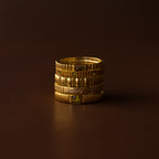 The Dainty Ribbed Peridot Ring, featuring a delicate ribbed design and a sparkling peridot gemstone, is stacked with engraved gold rings against a dark brown background.