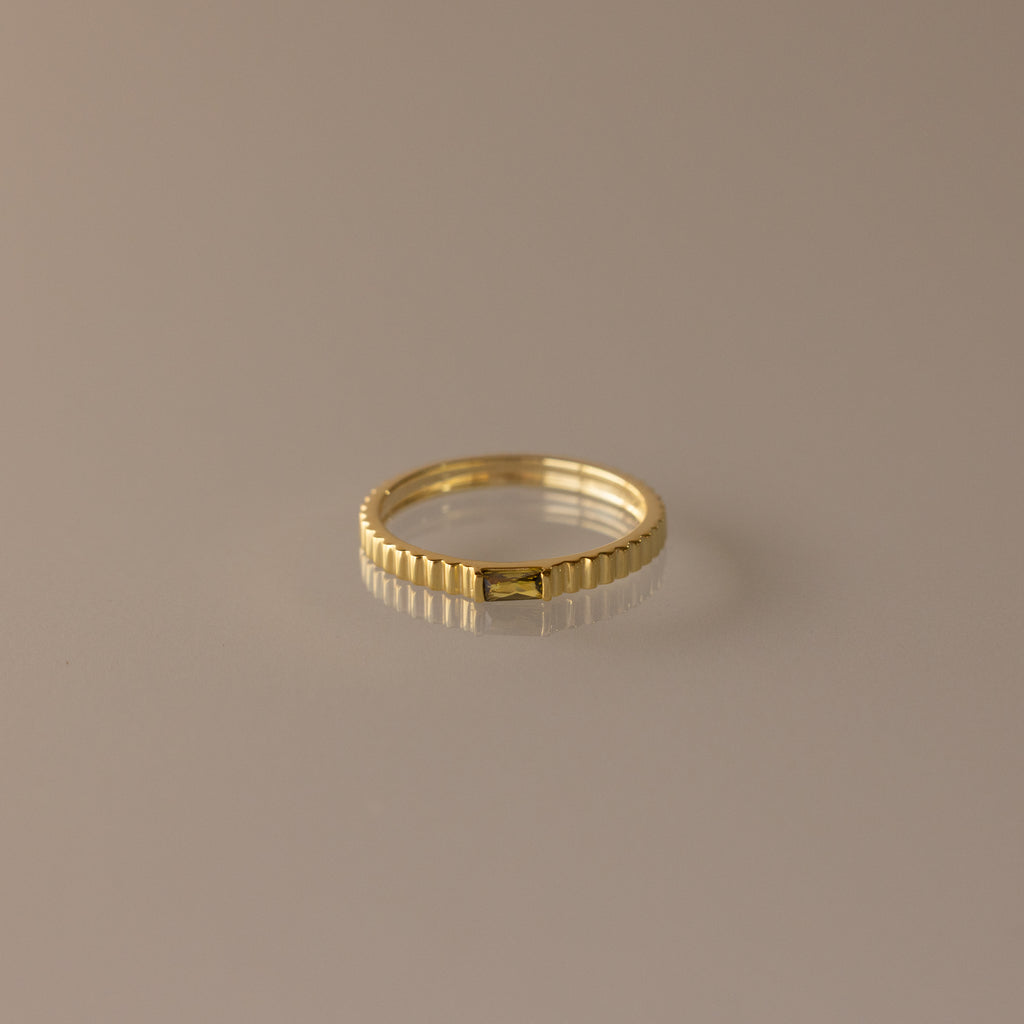 The Dainty Ribbed Peridot Ring features a gold, ribbed design and a minimalist look, displayed on a neutral background—perfect for stacking and adding elegant style to any outfit.