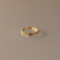 The Dainty Ribbed Amethyst Ring features a gold ribbed band and a small rectangular purple amethyst, perfect for stacking or as a delicate birthstone ring. Shown on a neutral background.