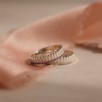 The Ribbed Blue Zircon Stack Ring rests on soft pink fabric with a blurred background, showcasing its stylish grooved edges—perfect for stacking or wearing as a statement piece.