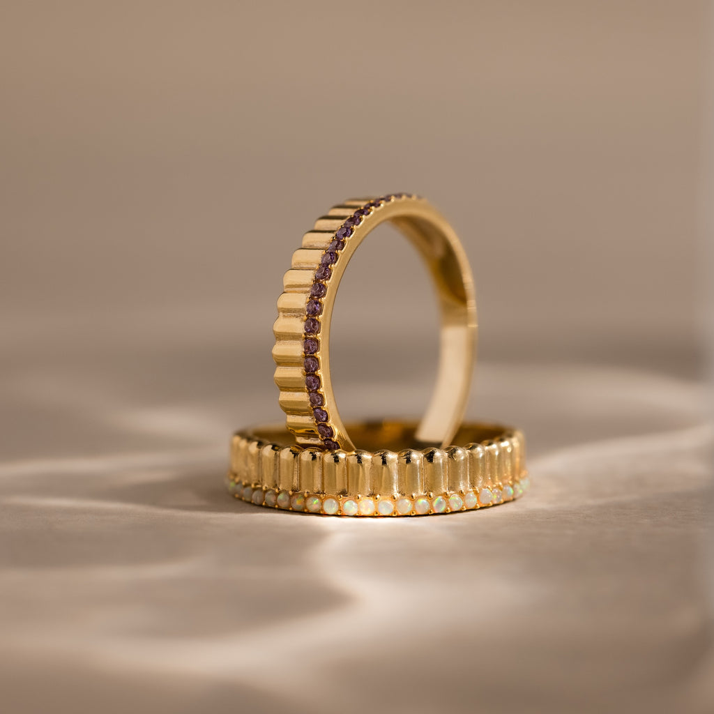 The Ribbed Birthstone Stack Ring features a gold band with ribbed texture and sparkling gemstones, displayed upright on a neutral surface—ideal for stacking as a unique birthstone ring set.