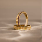 The Ribbed Birthstone Stack Ring features a gold band with ribbed texture and sparkling gemstones, displayed upright on a neutral surface—ideal for stacking as a unique birthstone ring set.