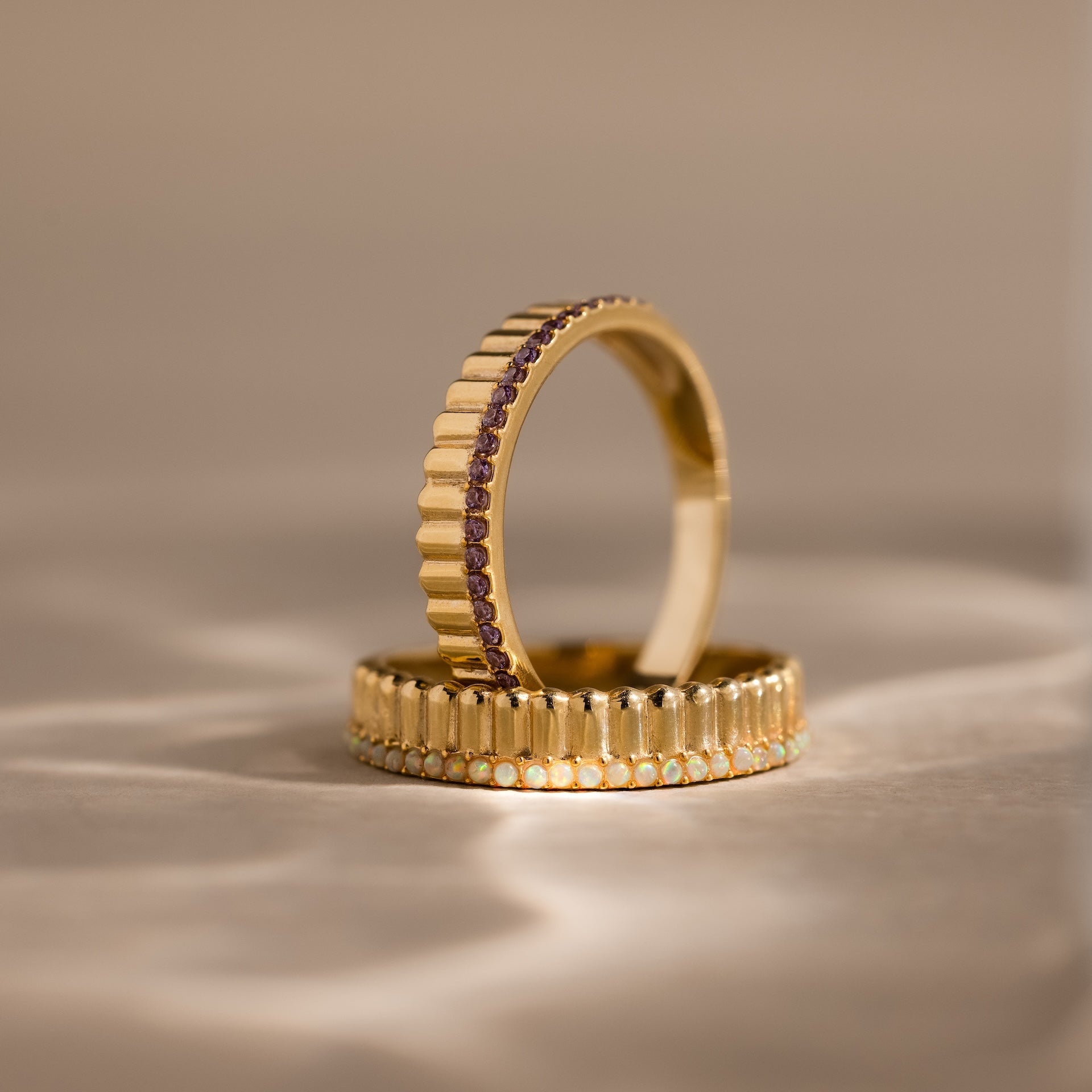 The Ribbed Birthstone Stack Ring features a gold band with ribbed texture and sparkling gemstones, displayed upright on a neutral surface—ideal for stacking as a unique birthstone ring set.